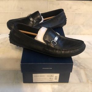 Cole Haan men’s black leather loafers with silver metal ornamentation on top.